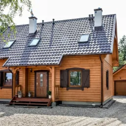 Drewniany dom z brązowym dachem, dwoma kominami i garażem w stylu rustykalnym, otoczony zielenią.