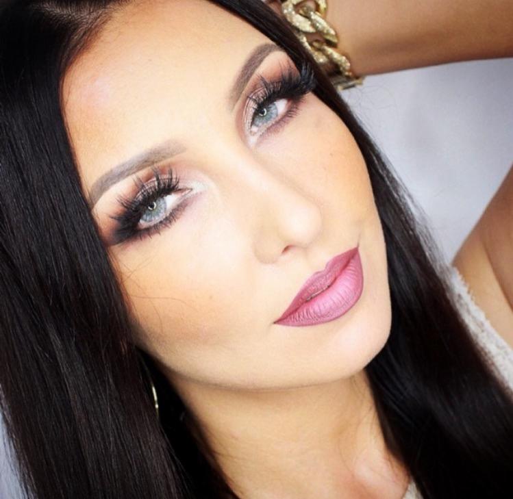 Portret kobiety z wyraźnie podkreślonymi oczami, sztucznymi rzęsami i matową pomadką w odcieniu mauve, z widoczną złotą bransoletą na nadgarstku.