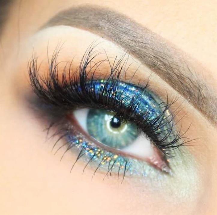 Zbliżenie na oko z intensywnym, błyszczącym, niebiesko-zielonym cieniowaniem i długimi, sztucznymi rzęsami, prezentujące efektowny, wieczorowy wygląd.