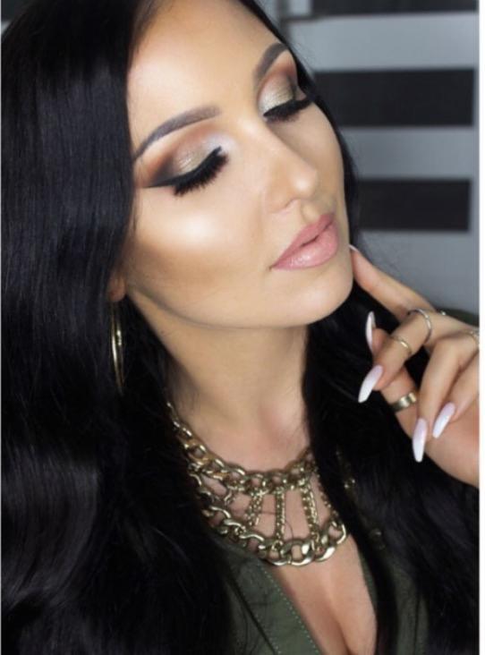 Portret kobiety z mocnym konturowaniem twarzy, złotym cieniem na powiekach i czarnym eyelinerem, podkreślone usta, długie białe paznokcie, złota biżuteria na szyi.