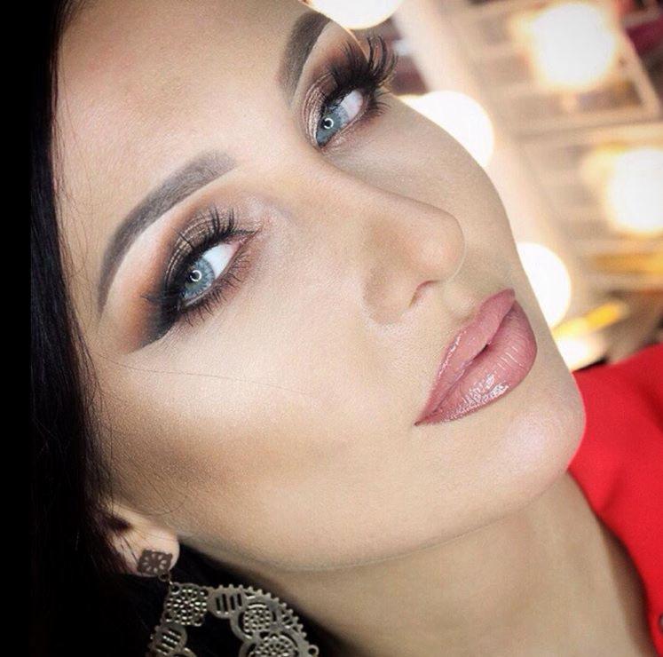 Portret kobiety z intensywnym brązowym cieniowaniem powiek, sztucznymi rzęsami i błyszczącymi, jasnoróżowymi ustami, widoczne duże kolczyki w stylu vintage.