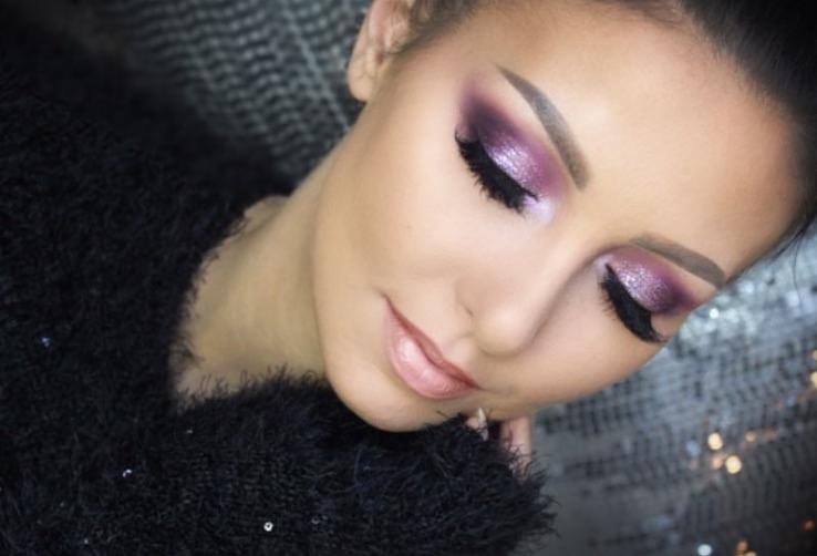Portret kobiety z zamkniętymi oczami, prezentującej fioletowy cień do powiek z brokatem i sztuczne rzęsy, delikatny róż na ustach i wyprofilowane brwi.