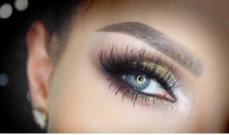 Zbliżenie na oko z intensywnym, złotym cieniowaniem, podkreślonymi rzęsami i wyraźnie zaznaczoną brwią.