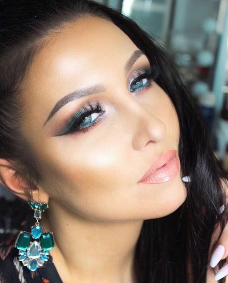 Portret kobiety z intensywnym, wieczorowym zdobieniem powiek w odcieniach turkusu i zieleni, podkreślonym czarną kreską, oraz błyszczącymi, brzoskwiniowymi ustami i dużymi, wiszącymi kolczykami...