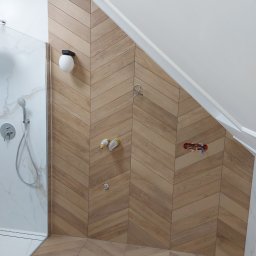 Przedsiębiorstwo usługowe Grzegorz Wądołowski - Nowoczesna łazienka na poddaszu z drewnopodobnymi płytkami ułożonymi w jodełkę na ścianie i podłodze. Widoczna kabina prysznicowa i przygotowane punkty instalacyjne.
