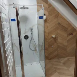 Nowoczesna kabina prysznicowa z deszczownicą, marmurowymi panelami i drewnopodobnymi płytkami ułożonymi w jodełkę w łazience na poddaszu.