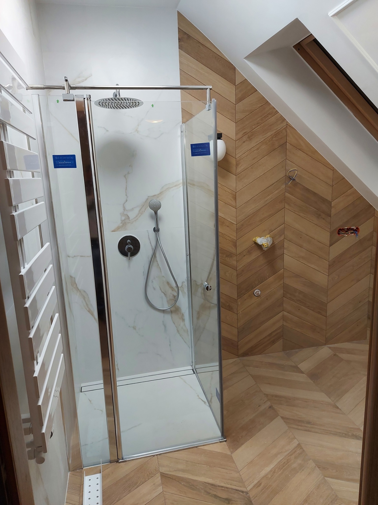Nowoczesna kabina prysznicowa z deszczownicą, marmurowymi panelami i drewnopodobnymi płytkami ułożonymi w jodełkę w łazience na poddaszu.