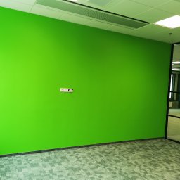 Mar-Bud - Świeżo pomalowana na jaskrawy zielony kolor ściana z widocznymi gniazdkami elektrycznymi w pustym biurze, widok na sufit kasetonowy i szklaną ścianę działową.