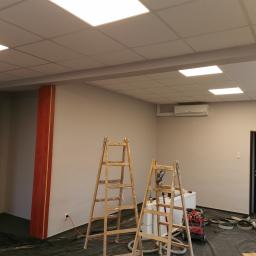 Mar-Bud - Montaż sufitu podwieszanego z oświetleniem rastrowym w pomieszczeniu w trakcie wykańczania w Krosinie, widoczne drabiny i narzędzia.