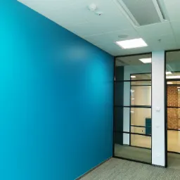 Ściana pomalowana na intensywny turkusowy kolor w nowoczesnym biurze z przeszkleniami w czarnych ramach i podwieszanym sufitem z oświetleniem.