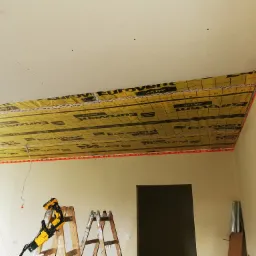 Montaż izolacji poddasza folią paroizolacyjną Eurovent Aktiv, widoczna konstrukcja sufitu z płyt kartonowo-gipsowych, drabiny i wkrętarka DeWalt przygotowane do dalszych prac.
