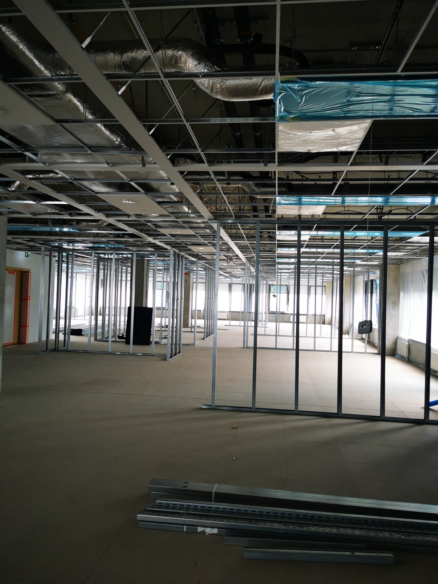 Stalowe profile konstrukcyjne ścian działowych w surowym stanie w nowo budowanym biurze, widoczne instalacje pod sufitem