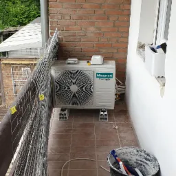 Zamontowana jednostka zewnętrzna klimatyzatora Hisense na balkonie, widoczny manometr i pompa próżniowa do serwisu, wiadro z narzędziami i fragment instalacji elektrycznej.