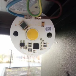 Podłączenie okrągłej płytki LED z elementami elektronicznymi i QR kodem do przewodów elektrycznych w obudowie lampy zewnętrznej.