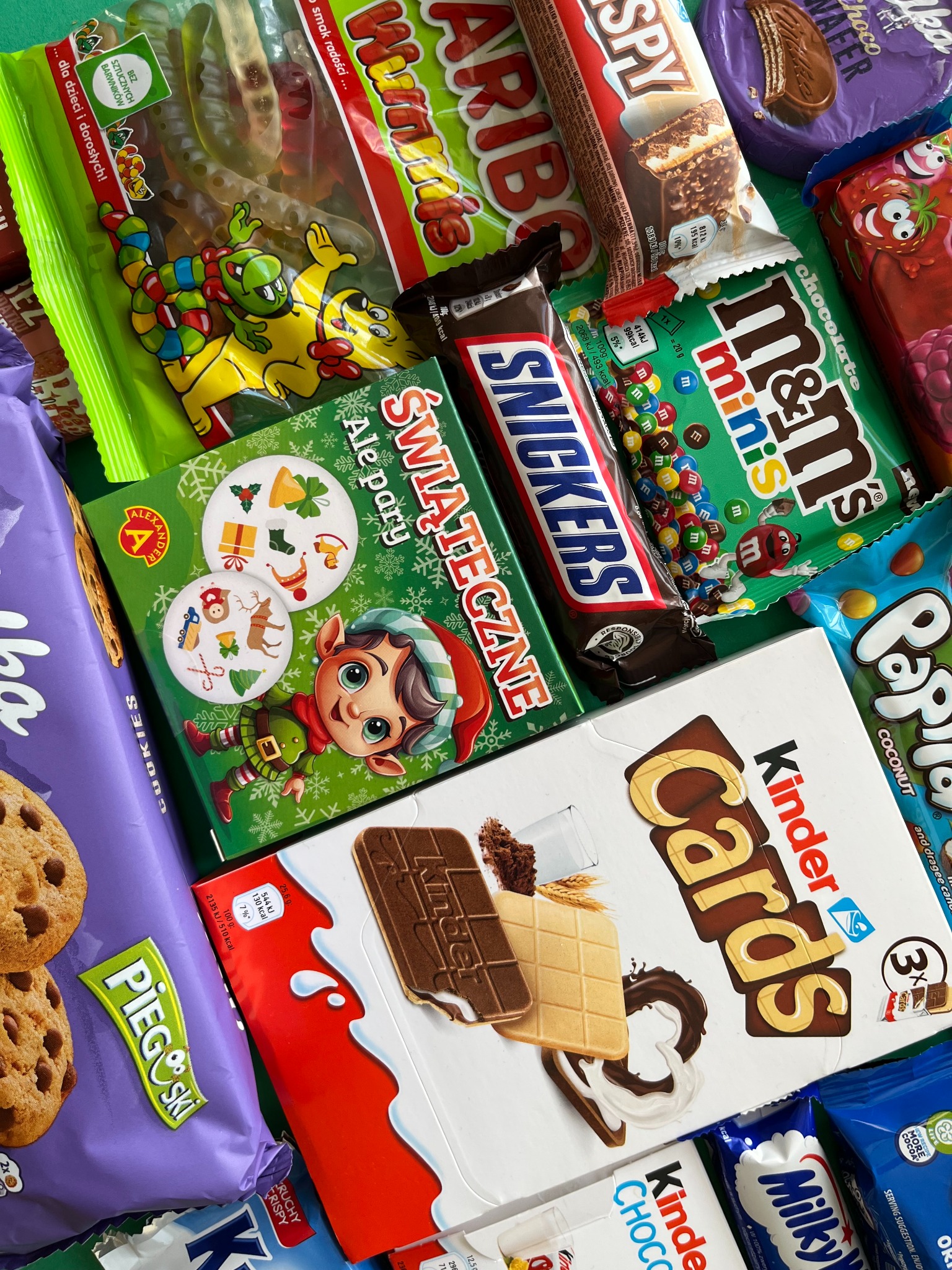Słodki asortyment: mieszanka batonów Snickers, M&M's Minis, Kinder Cards, żelków Haribo i ciasteczek Pieguski, idealna na prezent lub świąteczny poczęstunek.