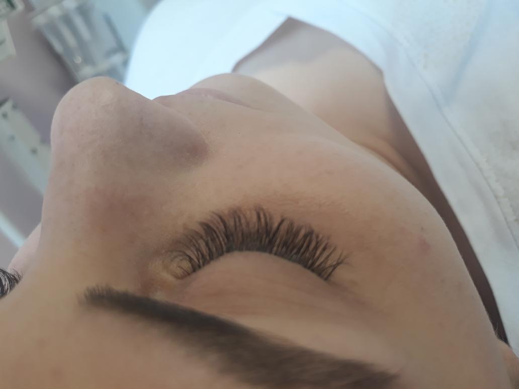 Zbliżenie na oko kobiety po zabiegu przedłużania rzęs, widoczne długie, gęste rzęsy oraz fragment brwi i nosa. Ujęcie z góry, w neutralnym oświetleniu.