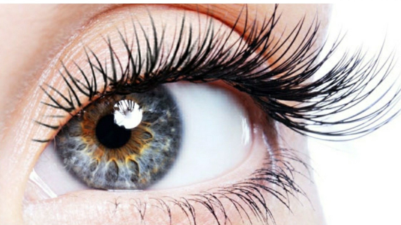 Zbliżenie oka z długimi, sztucznymi rzęsami; tęczówka szara z brązowym pierścieniem wokół źrenicy, widoczne drobne zmarszczki wokół oka.