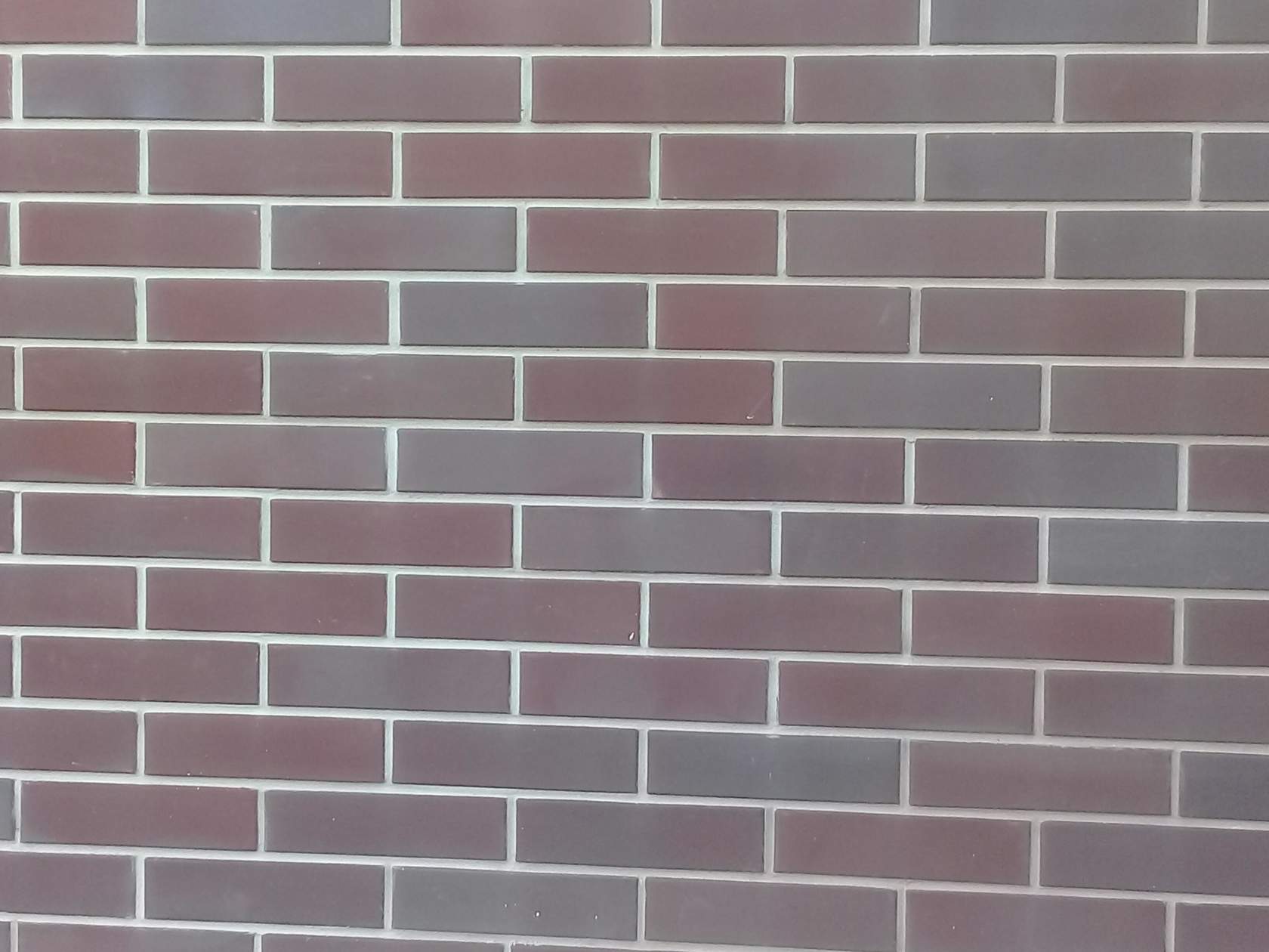 Elewacja z cegły klinkierowej w odcieniach czerwieni i szarości z jasną fugą, ułożona w regularny wzór.