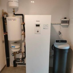 BUDOTOM SPÓŁKA Z OGRANICZONĄ ODPOWIEDZIALNOŚCIĄ - Biała pompa ciepła Panasonic Aquarea z zbiornikiem buforowym Perfekt Tank, orurowaniem i zmiękczaczem wody w pomieszczeniu z białymi płytkami.