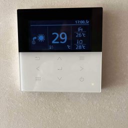 BUDOTOM SPÓŁKA Z OGRANICZONĄ ODPOWIEDZIALNOŚCIĄ - Nowoczesny panel sterowania klimatyzacją z czarną górą i białym dołem, wyświetlający temperaturę 29°C oraz inne parametry. Widoczne ikony i przyciski dotykowe.