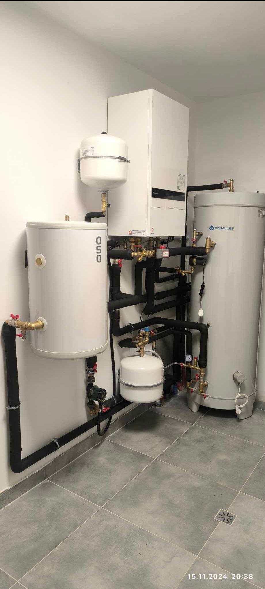 Zestaw urządzeń grzewczych: zbiorniki OSO i Coballes, rury z izolacją, armatura. Szara podłoga z odpływem. Gotowa instalacja w pomieszczeniu.