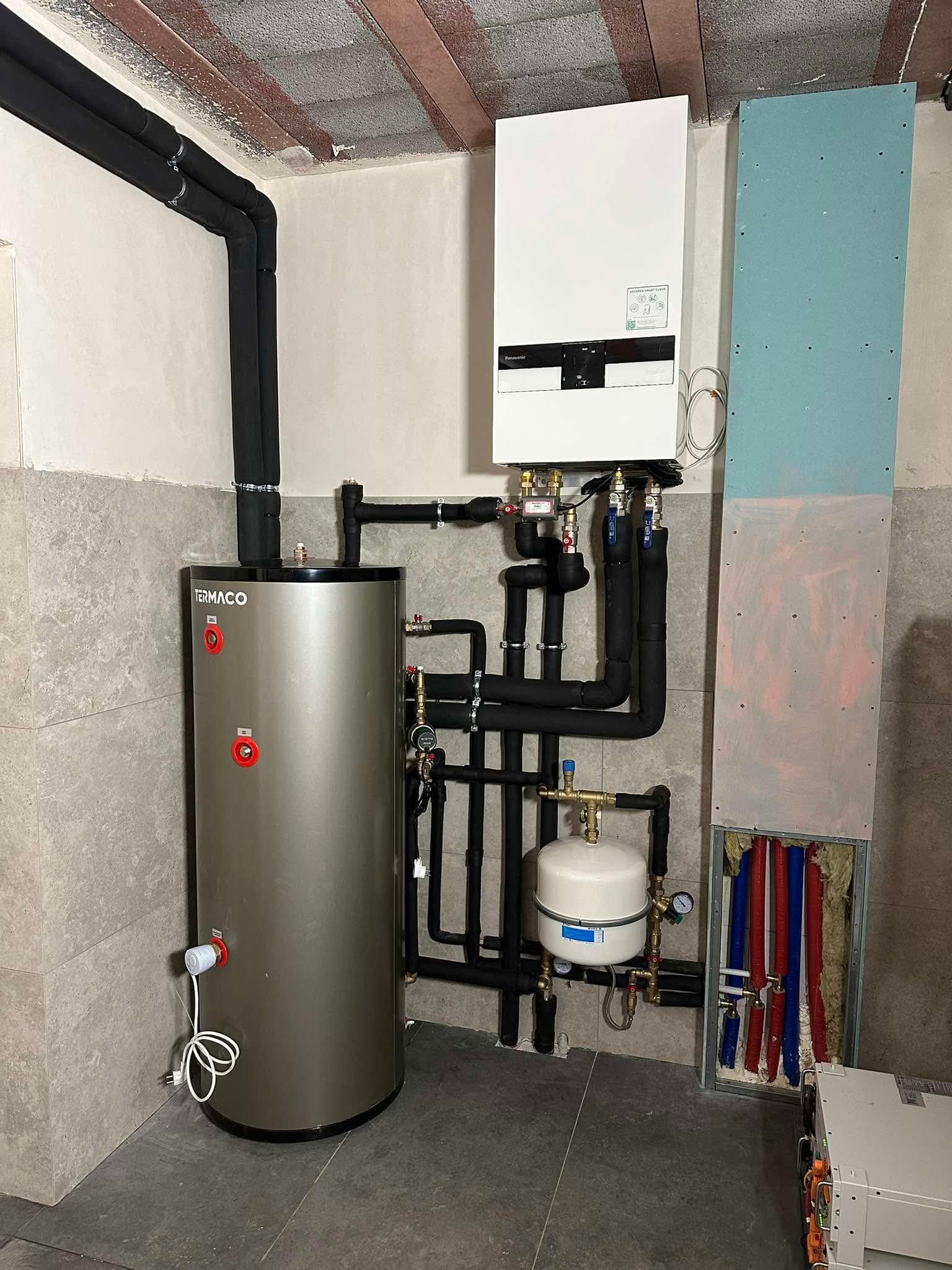 Instalacja grzewcza: bojler Termaco, piec Panasonic, rury w izolacji. Nowoczesna kotłownia z szarą płytką ścienną i drewnianym stropem.