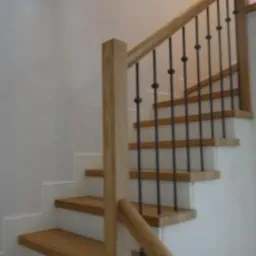 Jasne drewniane schody z czarnymi, metalowymi balustradami w nowoczesnym domu, widok z dołu.