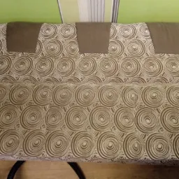 Sofa z tapicerką w brązowe i białe spirale, z trzema brązowymi zagłówkami, widoczne fragmenty podłogi i zielonej ściany.