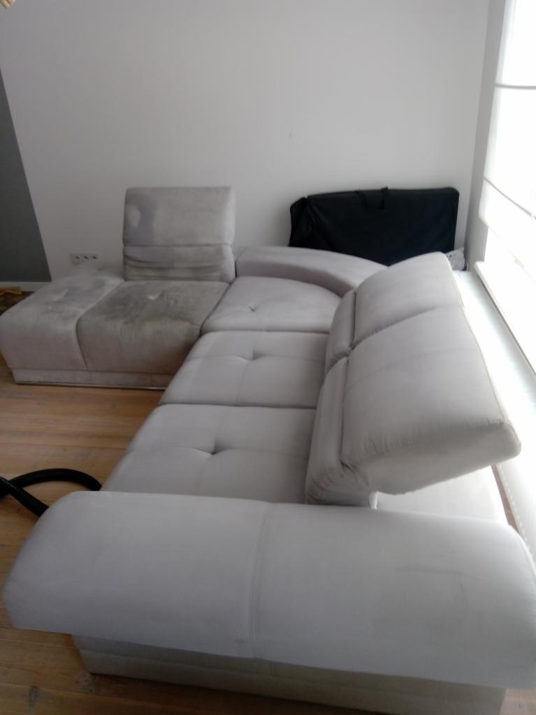 Jasnoszara, modułowa kanapa z widocznym fragmentem węża odkurzacza. Na jednym z modułów widoczne plamy, sugerujące etap czyszczenia tapicerki.