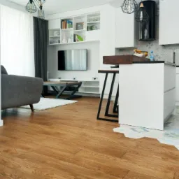 Salon z drewnianą podłogą ułożoną w jodełkę, przechodzącą w heksagonalne płytki pod wyspą kuchenną, widok zza progu.