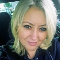 Portret uśmiechniętej blondynki w czarnej skórzanej kurtce, zrobiony wewnątrz samochodu, prawdopodobnie zdjęcie profilowe.