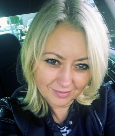 Portret uśmiechniętej blondynki w czarnej skórzanej kurtce, zrobiony wewnątrz samochodu, prawdopodobnie zdjęcie profilowe.