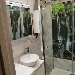 Przedsiębiorstwo usługowo handlowe - Wykończona łazienka z kabiną prysznicową z motywem wodospadu, umywalką nablatową i pralką.