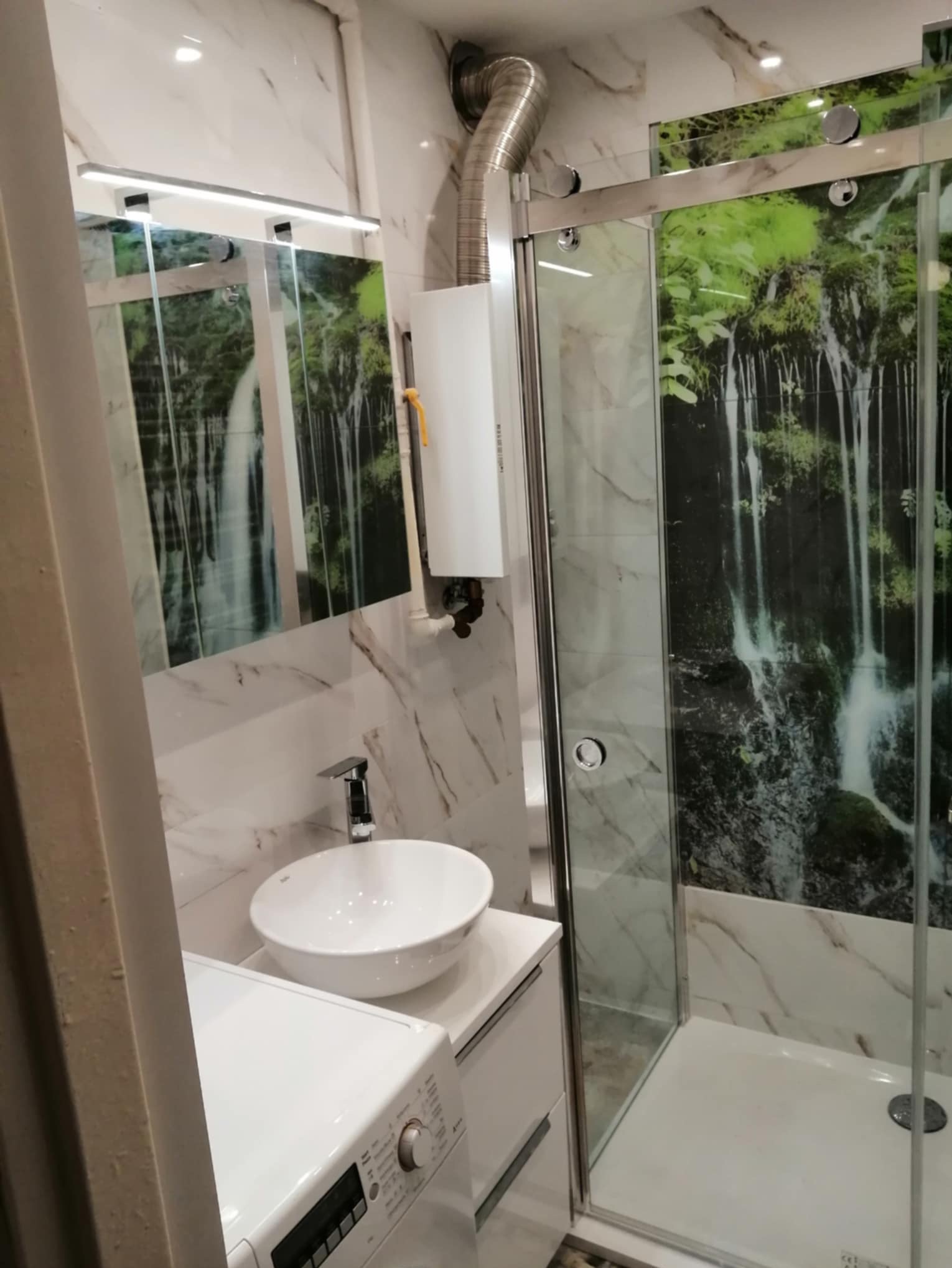 Wykończona łazienka z kabiną prysznicową z motywem wodospadu, umywalką nablatową i pralką.