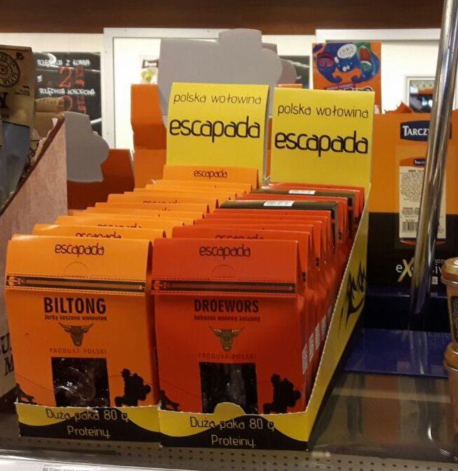 Półka sklepowa z opakowaniami suszonej wołowiny 'Escapada' w dwóch wariantach: Biltong i Droewors, z wyraźnym napisem 'Produkt Polski' i symbolem byka.
