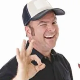 Uśmiechnięty mężczyzna w czarnej koszuli i czapce z daszkiem, mrużący oko i pokazujący gest 'OK' na jasnym tle.