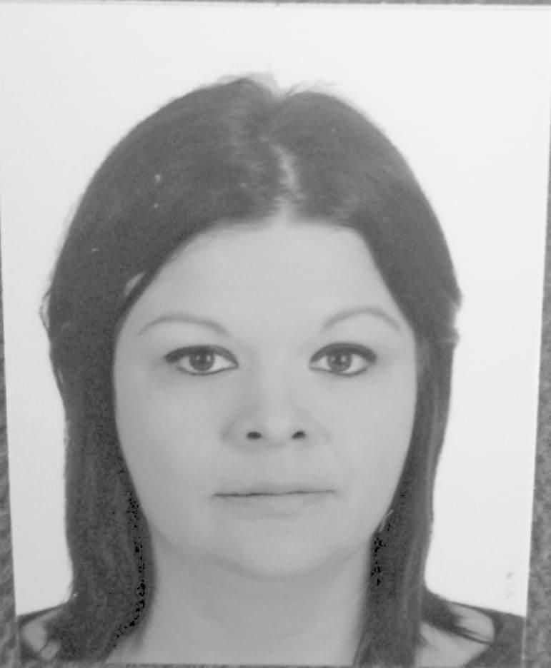 Czarno-biały portret kobiety o ciemnych włosach, z delikatnym uśmiechem, skierowana centralnie do kamery, na jasnym tle.