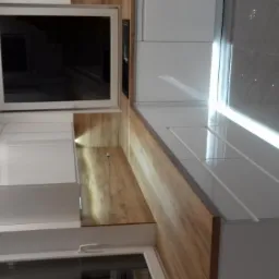 Nowoczesna kuchnia z białymi szafkami i drewnianym blatem, widok z dołu, podkreślony przez oświetlenie punktowe i błyszczące płytki podłogowe.