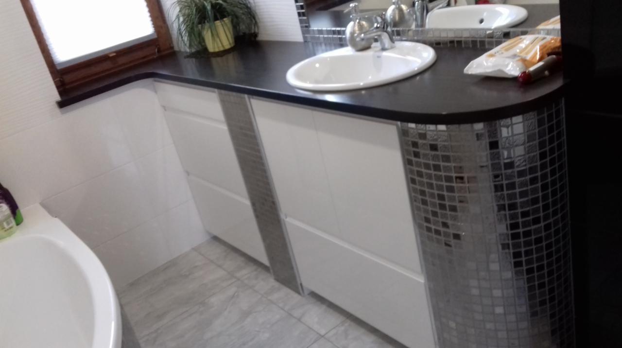 Łazienka z umywalką nablatową na czarnym blacie z białymi szafkami zdobionymi srebrnymi mozaikami, widok z boku na zaokrąglony fragment blatu.