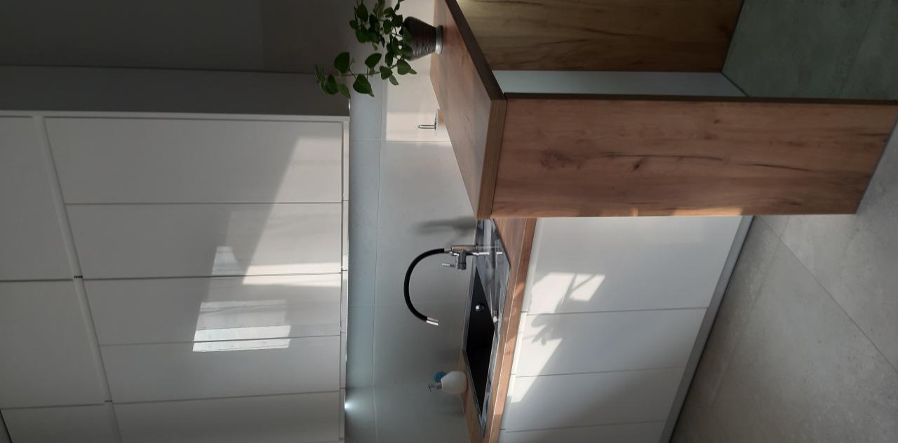 Nowoczesna kuchnia: białe, lakierowane fronty szafek dolnych, drewniany blat z rośliną w doniczce, czarny zlew z elastyczną wylewką.