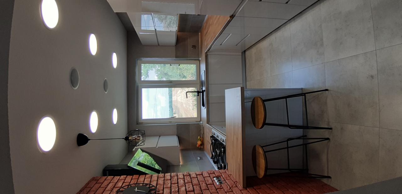 Nowoczesna kuchnia z ceglanym blatem, okrągłymi lampami w suficie i drewnianymi stołkami barowymi.