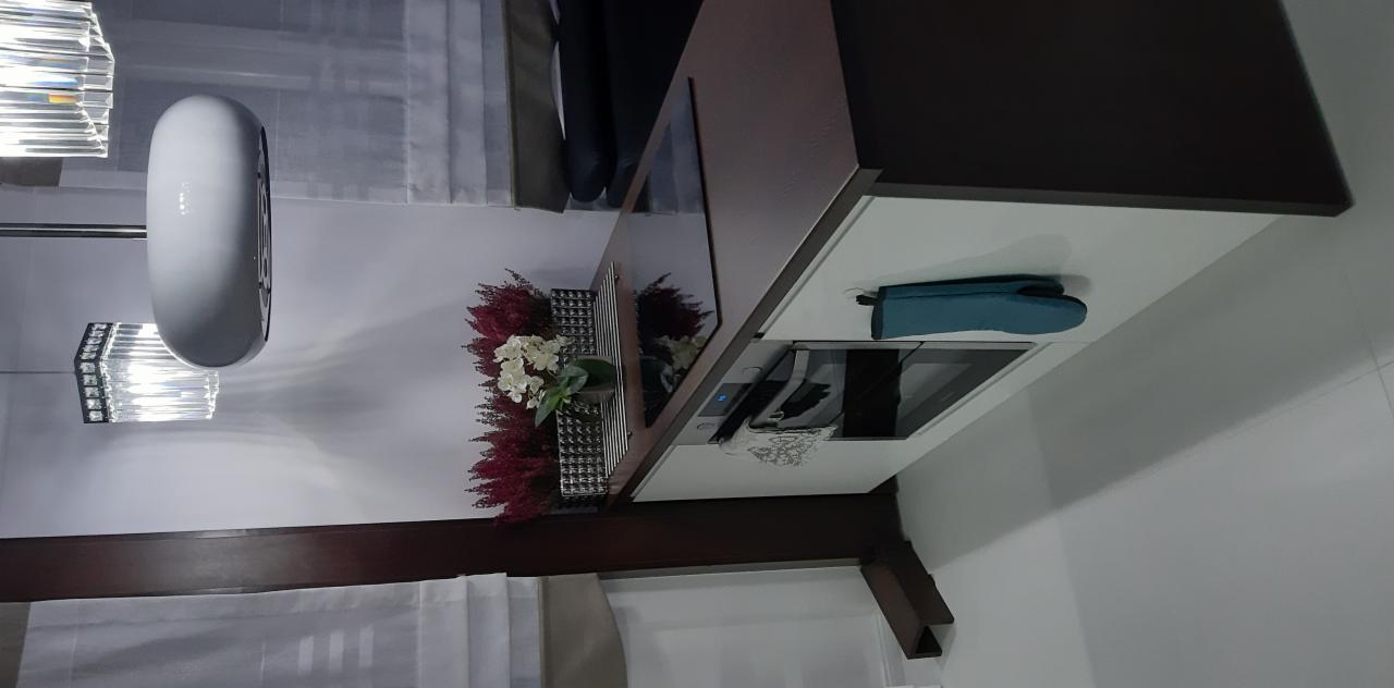 Fragment nowoczesnej kuchni z brązowo-białymi szafkami, kwiatami w wazonie na blacie i niebieską rękawicą kuchenną obok płyty indukcyjnej.