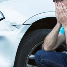 Kancelaria Prawna Solace - Zrozpaczony mężczyzna kuca obok uszkodzonego, srebrnego samochodu. Wgnieciony błotnik i reflektor sugerują kolizję. Emocje podkreślają potrzebę wsparcia prawnego.