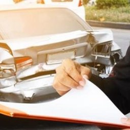 Kancelaria Prawna Solace - Mężczyzna w garniturze z dokumentami przy uszkodzonym samochodzie. Likwidacja szkody komunikacyjnej, ocena uszkodzeń pojazdu po kolizji.