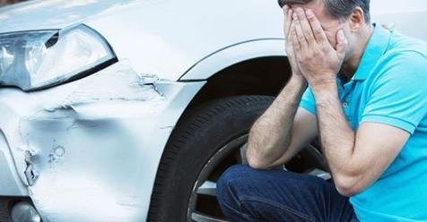 Zrozpaczony mężczyzna kuca obok uszkodzonego, srebrnego samochodu. Wgnieciony błotnik i reflektor sugerują kolizję. Emocje podkreślają potrzebę wsparcia prawnego.