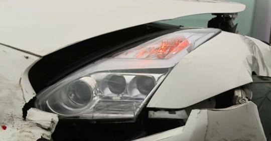 Uszkodzony przód białego samochodu z widocznym reflektorem i zniszczonym zderzakiem. Szkoda komunikacyjna, potencjalna sprawa odszkodowawcza.