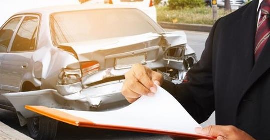 Mężczyzna w garniturze z dokumentami przy uszkodzonym samochodzie. Likwidacja szkody komunikacyjnej, ocena uszkodzeń pojazdu po kolizji.