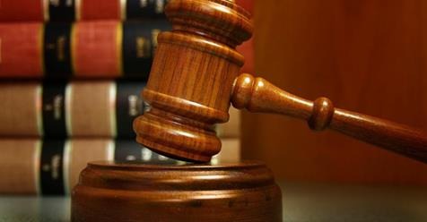 Drewniany młotek sędziowski na podstawie, obok stos książek prawniczych. Ciepłe oświetlenie, bliski plan, symbol sprawiedliwości i prawa.