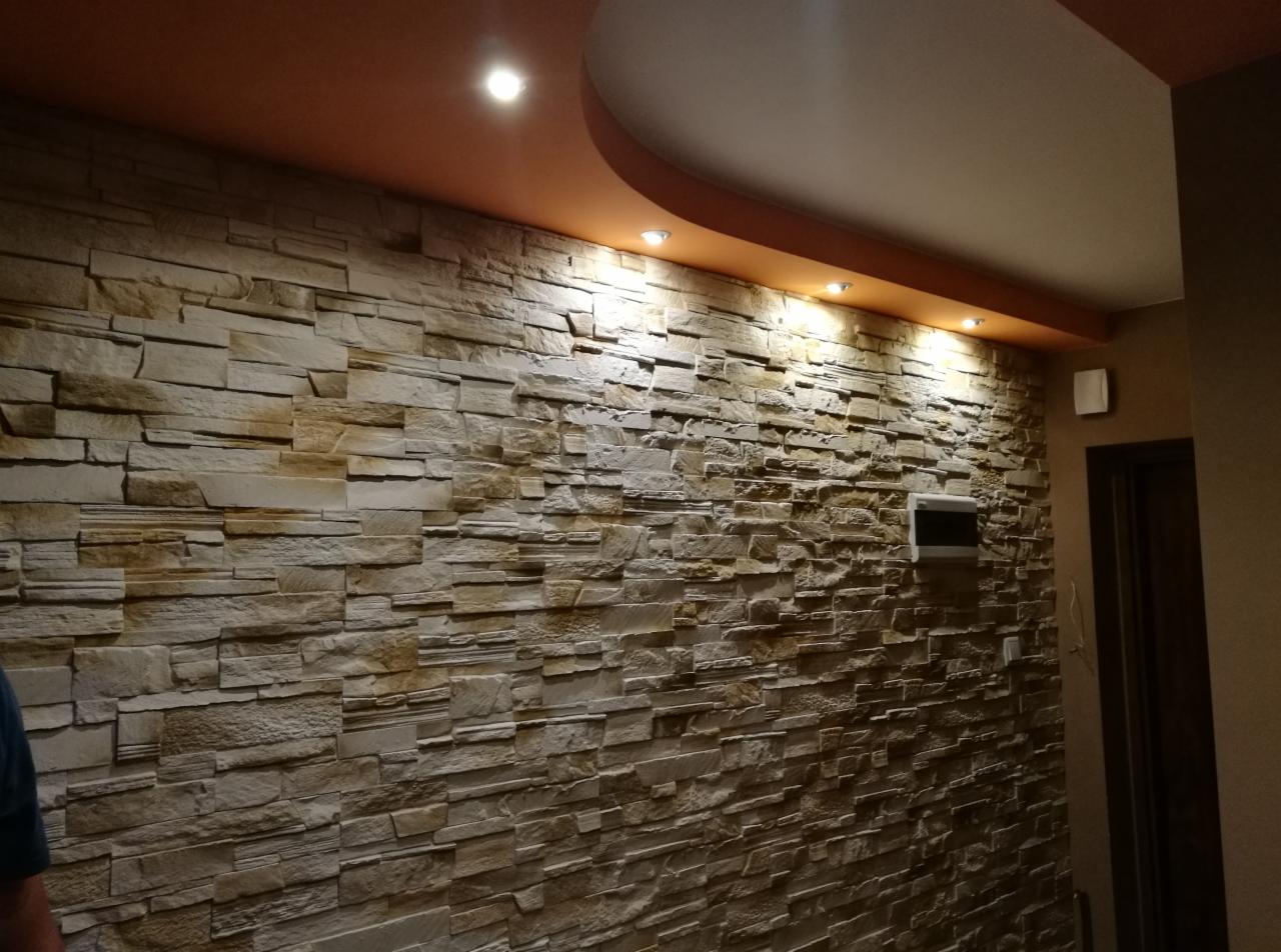 Ściana wykończona dekoracyjnym kamieniem w odcieniach beżu i brązu, z oświetleniem punktowym w suficie podwieszanym w Bilczy. Widoczna instalacja elektryczna.