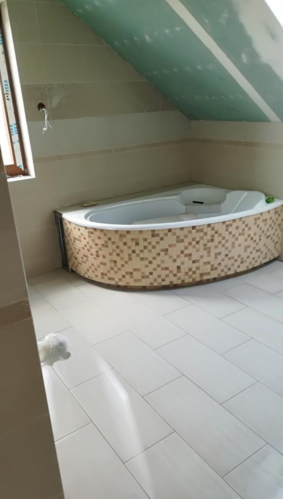 Wanna narożna obudowana mozaiką w łazience na poddaszu, białe płytki podłogowe, sufit z płyt karton gips.